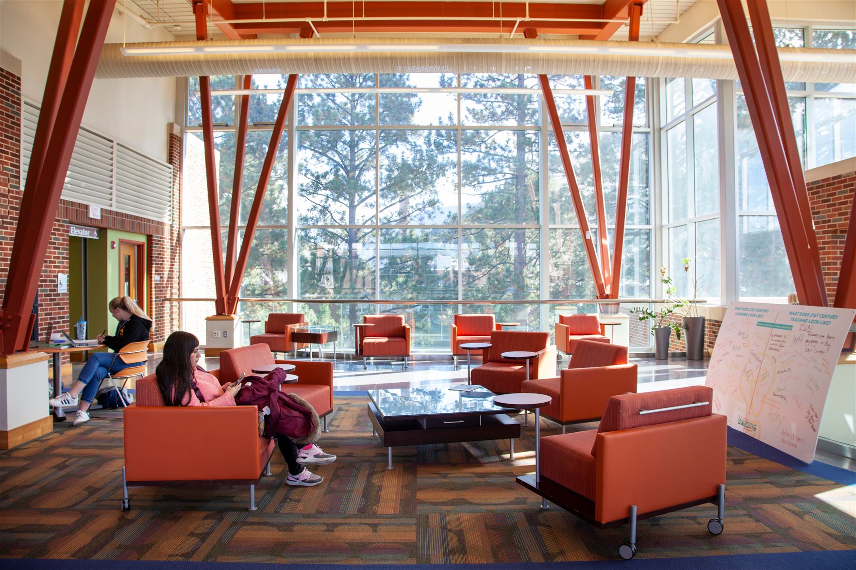 two students sitting in a lounge area of the college of eduction building in front of a large bank of windows